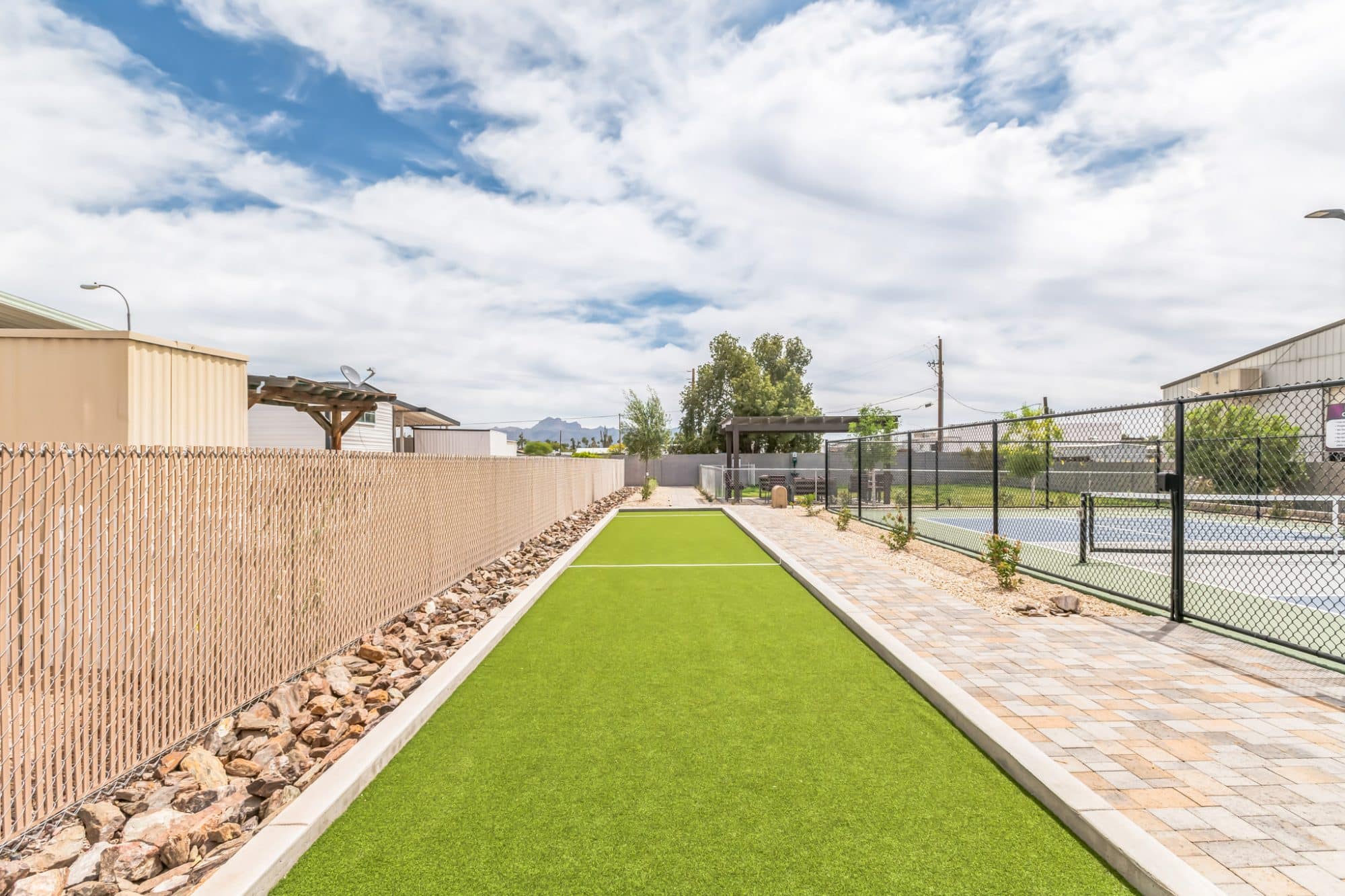 A bocce ball court with artificial turf, bordered by fencing and paved walkways on a sunny day in apache junction az