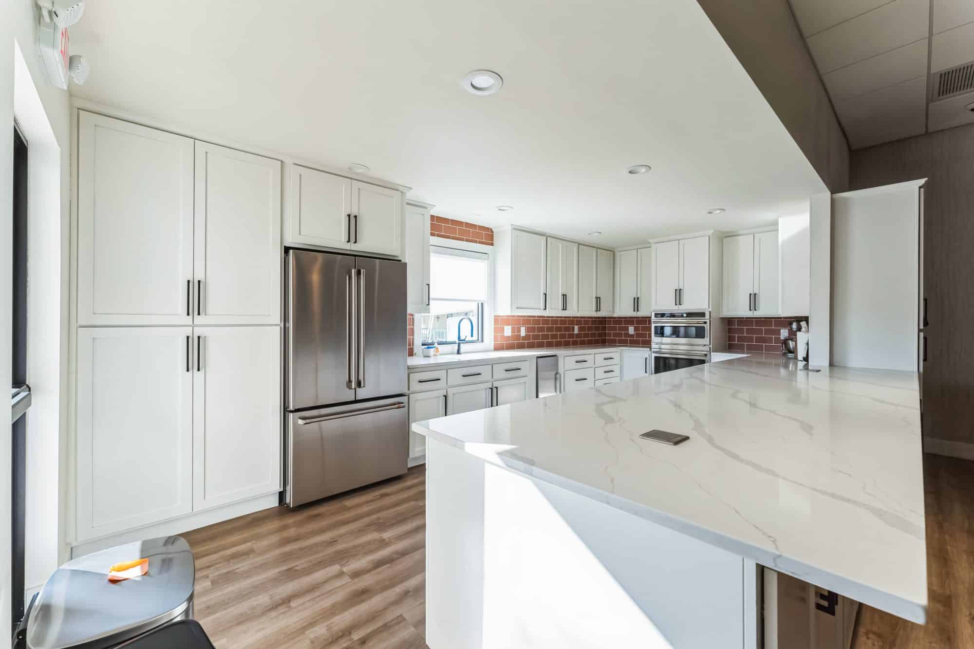 Spacious kitchen with white cabinetry, stainless steel appliances, a large island, and a red brick backsplash near Mesa, AZ