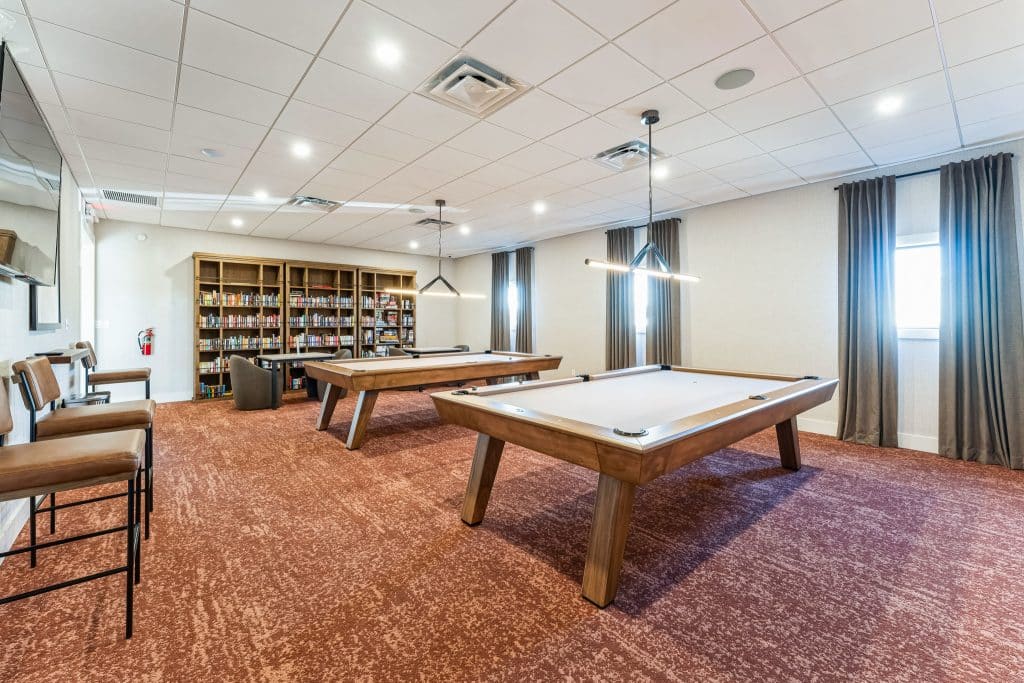 Another view of the recreation room, showing two pool tables, a library, and seating areas under bright lighting in apache junction az